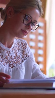 Öğrenci bir kütüphanede okurken, öğrenim ve eğitime odaklanarak kitap veya yayın yapıyor. Edebiyat, eğitim ve bilgiye adanmışlık. Dikey video.