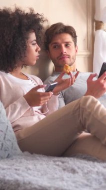 Yatak odasındaki aile çifti çevrimiçi eğlence için cep telefonu kullanıyor. Dijital haz odaklı karşılama ortamında sabah rahatlığı. Dikey video.