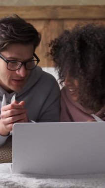 Çiftler hafta sonunu evde dizüstü bilgisayarlarında çeşitli online eğlencelerle eğlenerek geçirirler. Rahat bir ortam, hafta sonları mükemmel vakit geçirdiklerini gösteriyor. Dikey video.