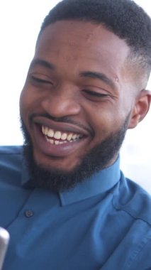 Mutlu Afro-Amerikan erkeği evde bir tabletle sosyal medyada sohbet ederek internet eğlencesini seviyor. Mutluluk, iletişim ve rahatlık. Dikey video.