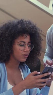 Mutlu ve tatmin olmuş iş arkadaşları ofiste birlikte bir iş molası verip telefonları online eğlence ve rahatlama için kullanıyorlar. Dikey video.