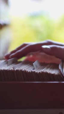 Öğretmen bir kart kataloğuyla çalışıyor, kütüphanede belge arıyor. Depolama, organizasyon ve eğitime adanmışlık. Dikey video.