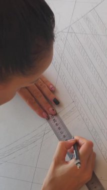 Terzi bir atölyede kıyafet eskizi hazırlıyor, dikiş ve imalata odaklanıyor. Meslek ve zanaatkarlık. Dikey video.