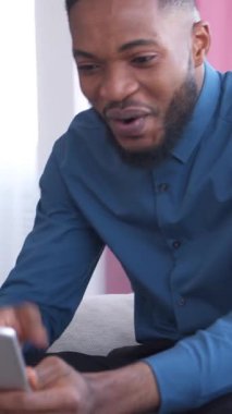 Dost canlısı Afro-Amerikan bir adam online eğlence ve evde zaman geçirmek için bir tablet kullanıyor. Rahatlama, teknoloji ve pozitif bir atmosfer. Dikey video.