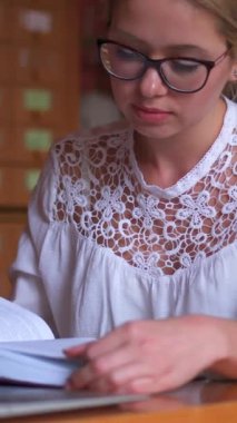 Kütüphanede kitap okuyan kadın öğrenci, öğrenme ve eğitime odaklanıyor. Bilgi, edebiyat ve kendini çalışmaya adamak. Dikey video.