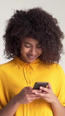 Mutlu Afro-Amerikan kadınları online iletişim ve boş zamanlarında beyaz arka planda sohbet için akıllı telefon kullanırlar. Bağlantı ve teknoloji. Dikey video.