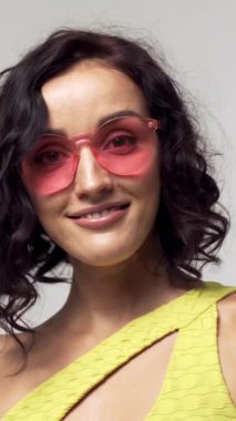 Beyaz bir arka planda sarı spor kıyafetli mutlu ve şık bir kadının portresi, eğleniyor. Canlı enerji ve bireysellik. Dikey video.