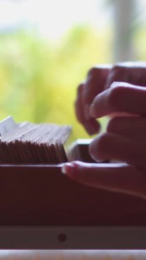 Kütüphane kartı kataloğu ya da arşivini inceleyen bir öğrencinin araştırma ve evrak işlerine odaklanması. Eğitim, organizasyon ve detaylara dikkat. Dikey video.