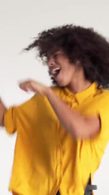 Neşeli ve heyecanlı Afrikalı Amerikalı kadın beyaz bir arka planda neşeyle dans ediyor, eğlence ve zevkle eğleniyor. Dikey video.