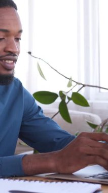Mutlu Afro-Amerikan ofis çalışanı evdeki online işler için dizüstü bilgisayar kullanıyor. İş hesaplarını planlayıp yönetiyor. Olumlu ve üretkenlik. Dikey video.