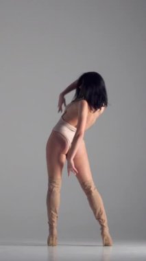 Şehvetli kadın dansçı, yüksek topuklularla beyaz bir arka planda, kendine güven ve kadınlık yayarak gösteri yapar. İlham, sanatçılık ve zarafet. Dikey video.