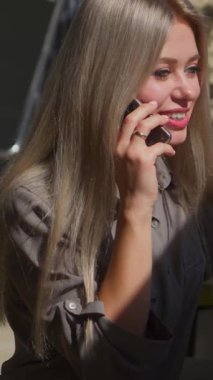 Dışarıda telefonla konuşan olumlu bir kadın. Çağrı sırasında konuşma ve iletişim kuruyor. Bağlantı, pozitiflik ve modern hayat. Dikey video.