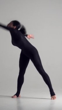 Etkin ve şık bir kadın dans ediyor ve beyaz bir arka planda geriniyor, modern dişiliği ve enerjiyi sergiliyor. Hareket, tarz ve zarafet. Dikey video.
