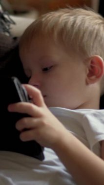 Neşeli küçük çocuk online eğlencenin tadını çıkarıyor ya da evdeki kanepede tabletle oyun oynuyor, neşe ve heyecan dolu. Dikey video.