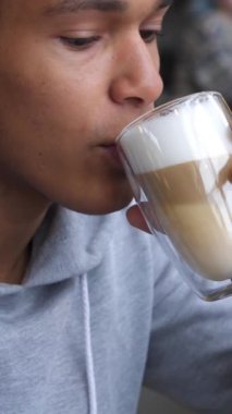 Afro-Amerikalı neşeli adam boş zamanlarını kafede kahve içerken internette geçiriyor. Rahatlama ve mutluluk. Dikey video.