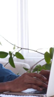 Neşeli afro-amerikan iş adamı bir sandalyeye yaslanıyor, iş molası sırasında ev ofisinde dinleniyor. Rahatlama ve pozitif bir iş hayatı dengesi. Dikey video.