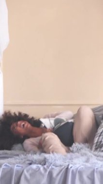 Oyuncu karı koca yatak odasında yastık savaşı yapıyor. Eğlence ve mutluluk, neşeli anlarda rahat boşluğu doldurur. Dikey video.