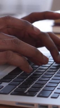 Ev ofisinde dizüstü bilgisayarla çalışan Afro-Amerikan bir Amerikalı 'nın yakın çekimi. Uzaktan çalışma, işgal ve iletişim. Dikey video.