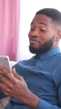 Pozitif Afro-Amerikalı bir adam online video görüşmesi için tablet kullanıyor ve evdeki arkadaşlarıyla konuşuyor. İletişim, bağlantı ve teknoloji. Dikey video.