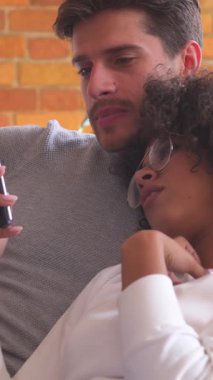 Mutlu aile çifti evde boş zamanlarını birlikte geçirir, telefonda eğlence ve rahatlama için internete bakarlar. Dikey video.