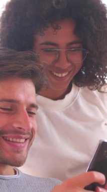 Neşeli aile çifti evde boş vakitlerini birlikte geçiriyorlar, online sosyal medya aktiviteleri ve eğlencenin tadını çıkarmak için telefon kullanıyorlar. Dikey video.