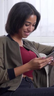 Neşeli Afro-Amerikan kadınları dijital eğlencelerini evde bir tablet bilgisayar, iletişim ve neşeli rahatlama kullanarak geçiriyorlar. Dikey video.