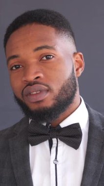 Siyah arka planda takım elbiseli, güler yüzlü, Afro-Amerikan bir adamın portresi. Bireysellik, tarz ve centilmence bir davranış. Dikey video.