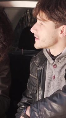 Rahat bir çift, dışarıda güzel bir sohbet ederken bir arabanın bagajında oturup, bir şişeden çay içmekten zevk alır. Dikey video.