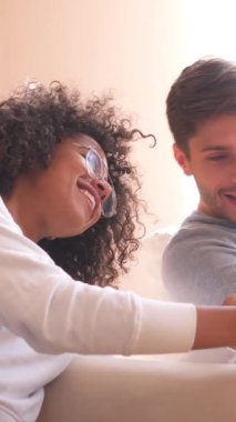 Aile çifti evde kaliteli zaman geçirir, online eğlence için telefon kullanır ve eğlencesini paylaşır. Dikey video.