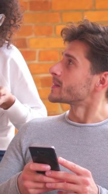 Arkadaş canlısı aile çifti evde vakit geçirip sohbet ederken internet aktiviteleri için telefon kullanıyor. Dikey video.