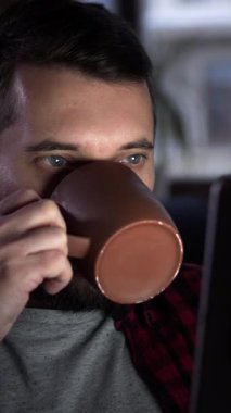 Pozitif adam evde çay içerken online eğlence için tablet bilgisayar kullanıyor. Sahne rahatlama ve dijital eğlenceyi birleştirir. Dikey video.