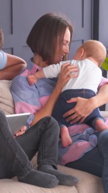 Mutlu aile boş zamanlarını evdeki kanepede birlikte geçirir, online eğlence için bir tablet bilgisayar kullanır. Neşe, birliktelik ve dijital eğlence. Dikey video.