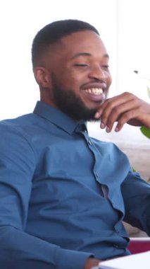 Keyifli Afro-Amerikan serbest çalışan bir vatandaşı, internet üzerinden yapılan bir video görüşmesi sırasında evde çalışırken konuşuyor. Boş zaman, iletişim ve uzaktan çalışma. Dikey video.