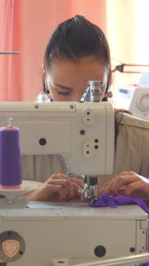 Kadın terzi, bir atölyede elbise ve dikiş makinesiyle çalışıyor. Yaratıcılık, işçilik ve dikiş işleme. Dikey video.