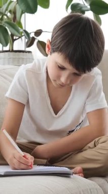 Ev ödevi için not defterine bir şeyler yazan okul çocuğu sakin bir çalışma ortamında konsantrasyonla e-öğrenme egzersizi yapıyor. Dikey video.