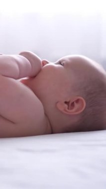 Bebek evde yatakta rahat bir şekilde uzanıyor, bebeklik keşfi sırasında oyun oynuyor ve dünyayı öğreniyor. Dikey video.