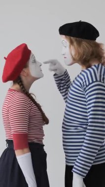 Kızgın pandomimci sanatçılar beyaz bir arka planda kavga ediyor, yoğun ve dramatik eylemlerle çatışma ve sorunları dile getiriyorlar. Dikey video.