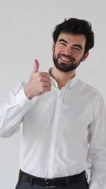 Neşeli bir adam beyaz bir arkaplanda olumlu ve iyi bir jest gösterir, başarıyı işaret eder, onay, onay ve memnuniyeti pozitif ve kendinden emin bir tavırla gösterir. Dikey video.