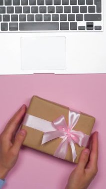 Pembe arka planda bir sürprizle hediye kutusunu sallayan kadın, merak ve heyecanı ifade ediyor, tebrik ve takdir için hazırlanıyor. Dikey video.