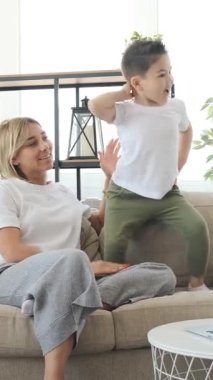 Memnuniyetle anne ve oğul dans ediyor ve evde müzikle eğleniyor, canlı bir eğlenceyle meşgul oluyor, canlı bir ev ortamında neşeli anılar yaratıyor. Dikey video.