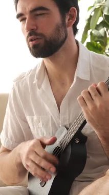 Evde boş zamanlarında gitarla müzik çalan, keyif alan ve rahatlatan sakin ve yaratıcı bir müzik deneyimi yaratan olumlu bir adam. Dikey video.