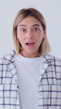 Şaşırmış ve afallamış bir kadın zafer kutlaması ya da beyaz arka planda şaşırmış bir ifadeyle iyi haberi haykırıyor. Dikey video.