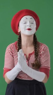 Gülümseyen pandomimci kadın yeşil arka planda memnuniyetle alkışlıyor, neşeli bir kutlama jesti ile tebrik ediyor. Dikey video.