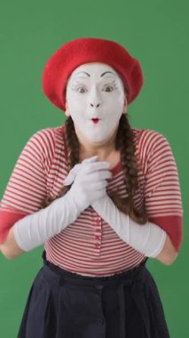 Heyecanlı pandomimci kadın yeşil arka planda şaşkınlıkla alkışlıyor ve güzel haberi coşkuyla kutluyor. Dikey video.