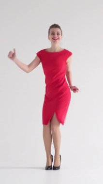 Aktif ve heyecanlı bir kadın, beyaz bir arka planda dans ederken, dinamik ve neşeli hareketlerle bir diskoteğin enerjisini somutlaştırıyor. Dikey video.