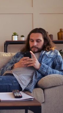 İnternet 'te boş vakit geçirmek ve evde sohbet etmek için telefon kullanan bir adam, siber uzay etkileşimleriyle rahat bir ortamda savaşarak can sıkıntısıyla mücadele ediyor. Dikey video.