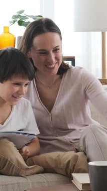 Memnuniyet duyan oğul ve anne evde bir not defterinde ödev yapıyorlar, destekleyici ve neşeli bir ortamda öğrenme ve eğitimi paylaşıyorlar. Dikey video.