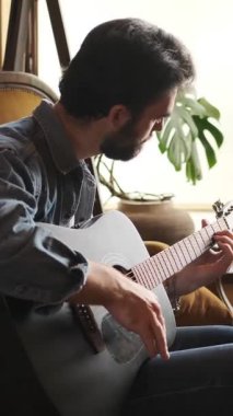 Boş zamanlarında evde gitar çalan olumlu bir adam, müzikte tatmin ve eğlence bulan, rahat ve rahat bir ortamda neşe saçan. Dikey video.