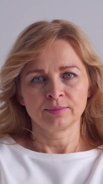 Beyaz bir arkaplanda ciddi ve gururlu bir kadın, düşünceli ve konsantre olmuş bir kişilik sergiliyor. Dikey video.