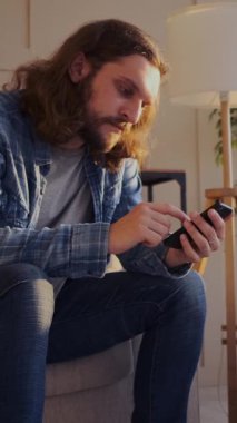 İnternette gezinmek ya da sosyal medyada sohbet etmek için telefon kullanan, rahat bir dijital ortamda odaklanmayla çevrimiçi etkileşime giren bir adam. Dikey video.